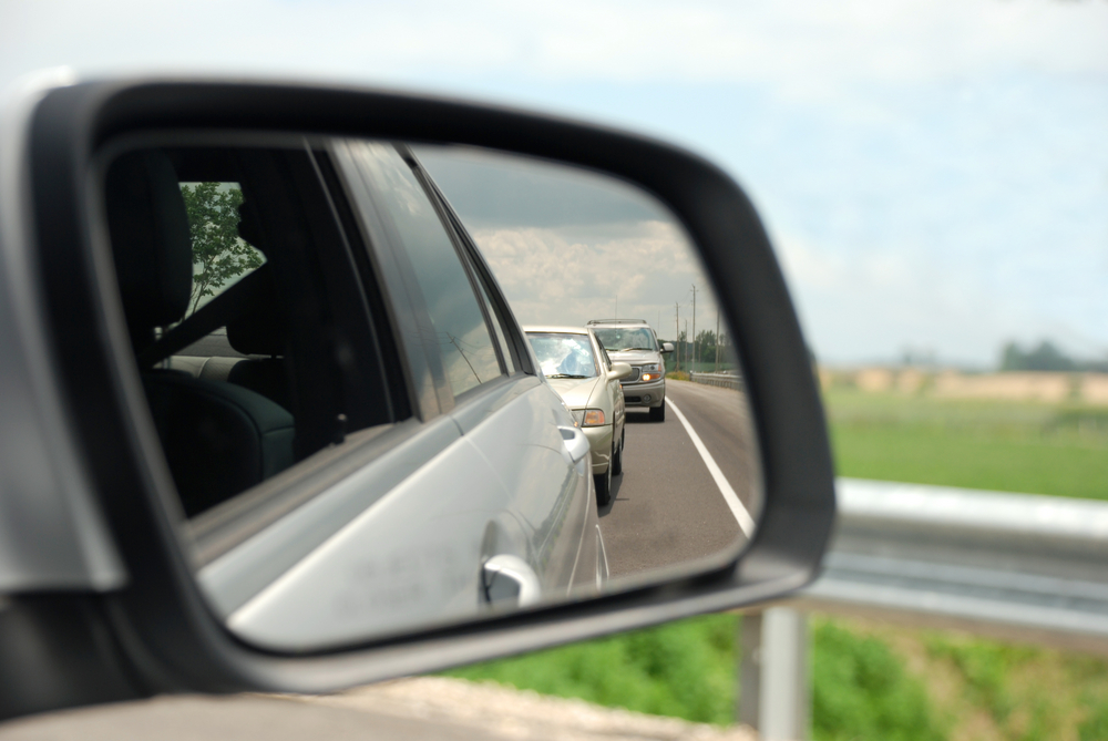 Vehicle's passenger side-view mirror with two vehicles in reflection following behind