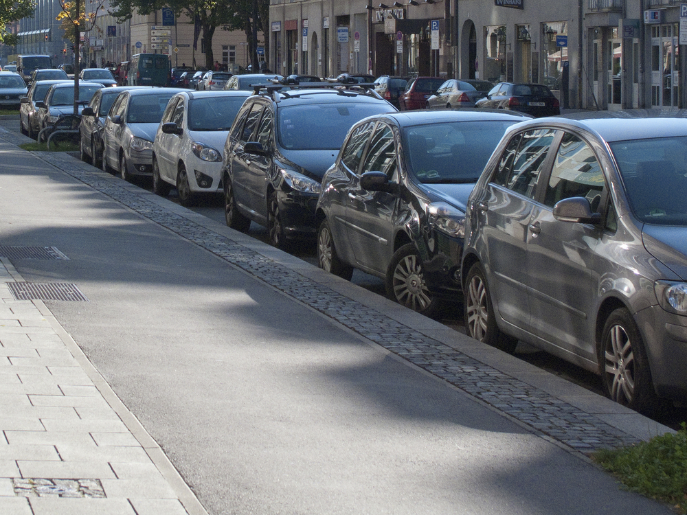 Line of cars parallel parked by urban sidewalk