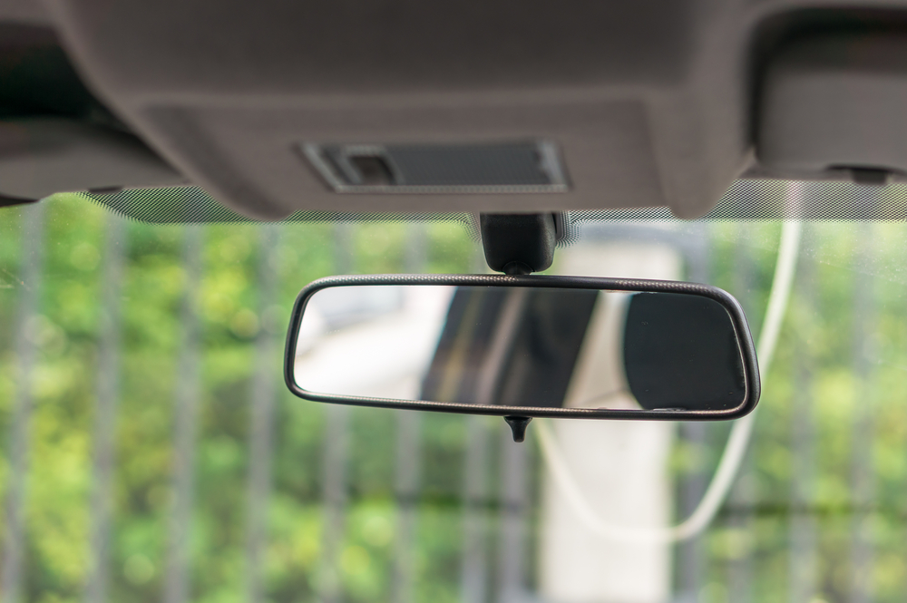 Rear view mirror in vehicle with blurred background of green trees and fence