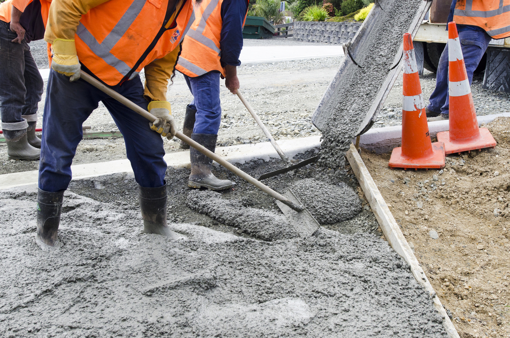 Road construction workers in orange vests using tools to smooth tar pouring from machine to put down new road