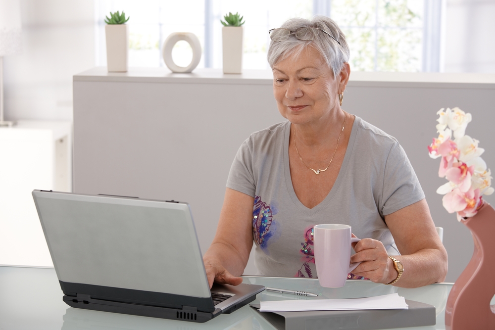Woman on laptop at desk with cup of coffee in one hand