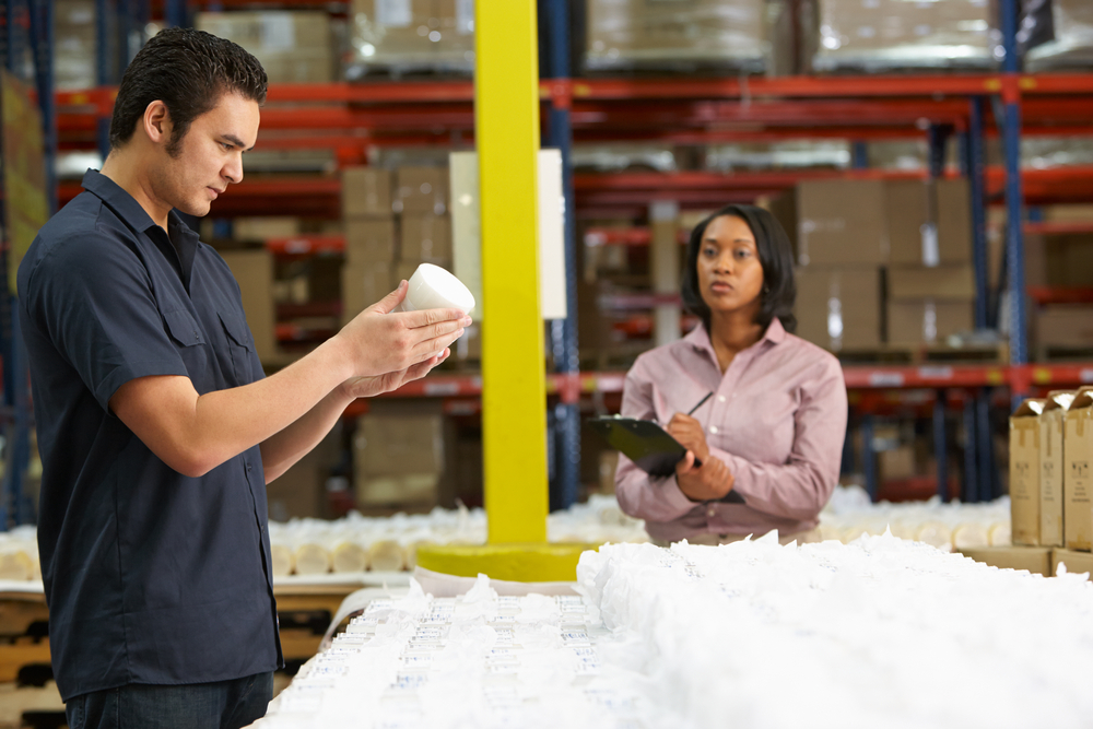 Man inspecting product for quality at warehouse with woman writing information on clipboard