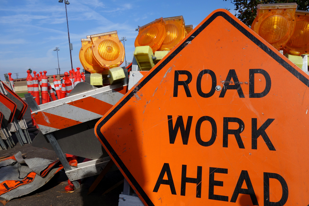 Road Work Ahead sign next to barriers with flashers on road with construction with beautiful blue sky and white whispy clouds