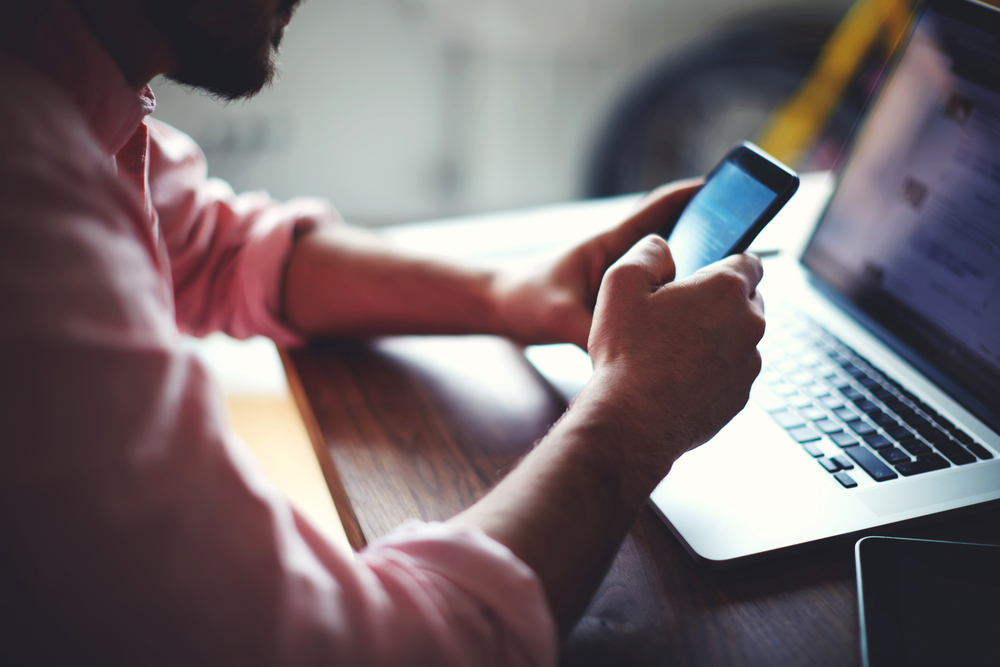 Man on smartphone in front of laptop and tablet