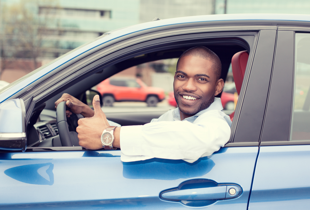Man in blue car smiling and giving a thumbs up